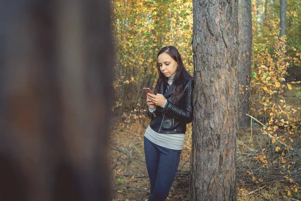 Frau benutzt im Herbstwald ein Smartphone. Weibchen wählt eine Nachricht am Telefon — Stockfoto