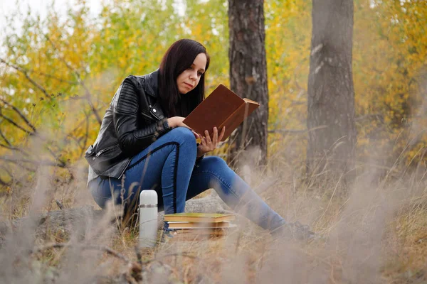 Belle femme lisant un livre dans la forêt d'automne. Une femme s'assoit près d'un arbre dans une forêt d'automne et tient un livre. Fille lisant un livre. Concept de la saison d'automne et lecture — Photo