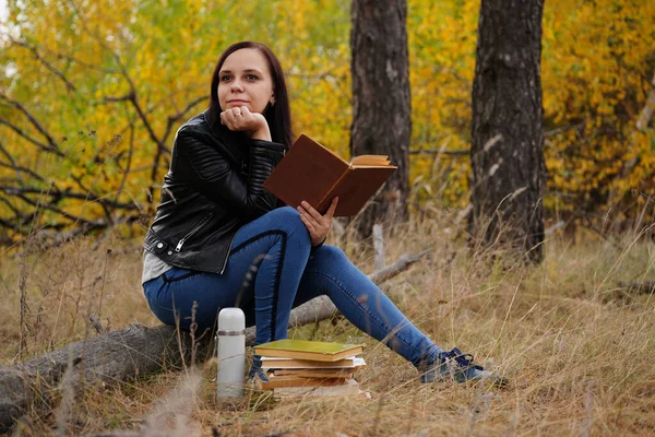 Belle femme lisant un livre dans la forêt d'automne. Une femme s'assoit près d'un arbre dans une forêt d'automne et tient un livre. Fille lisant un livre. Concept de la saison d'automne et lecture — Photo