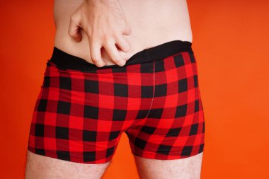 A man in red underpants on an orange background. Body parts: mens ass in underwear. Inflated buttocks in boxer shorts. Concept: diseases of the anus, constipation and male problems.