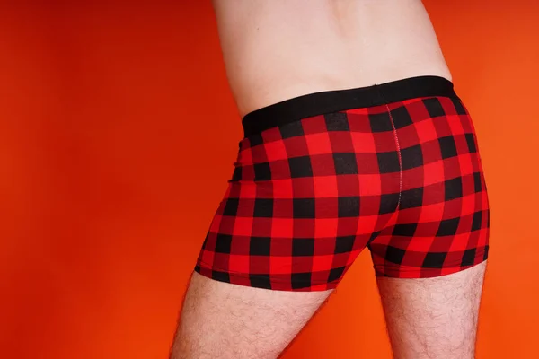 A man in red underpants on an orange background. Body parts: mens ass in underwear. Inflated buttocks in boxer shorts. Concept: diseases of the anus, constipation and male problems. — Stockfoto