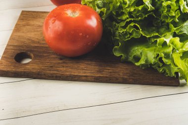 Su damlacıkları ve yeşil marullu kırmızı domatesler tahta bir tahtanın üzerinde..