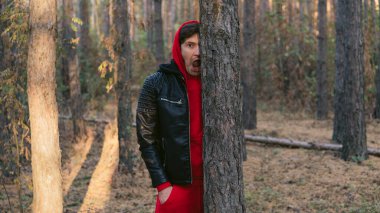 Genç yakışıklı bir adam sonbahar ormanında gün batımında yüzünü buruşturur..