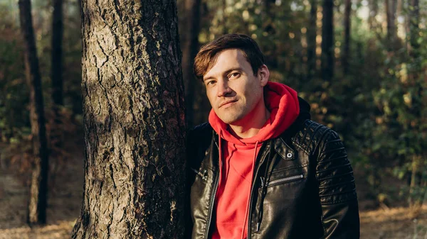 Un joven guapo se levanta en el bosque de otoño al atardecer. — Foto de Stock