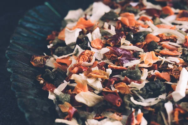 Seasoning a mix of dry vegetables in a plate on a black background. Especias y condimentos para cocinar — Foto de Stock