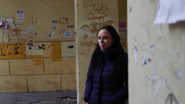 Una mujer hermosa se encuentra en el gueto, contra un muro doblado. Una chica vestida de calle se encuentra sola y mira hacia la distancia. Concepto: depresión y pobreza en Rusia — Vídeo de stock