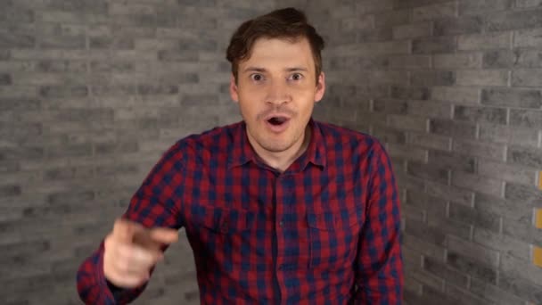 A young handsome man in a plaid shirt with bristles smiles and raises his index finger up from visited by inspiration on a brick background. The concept of great idea. — Stock Video