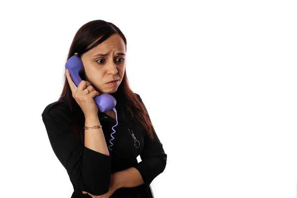 Uma mulher jovem bonita em um vestido preto escuta calmamente alguém no telefone home no fundo branco isolado. Copiar espaço. — Fotografia de Stock