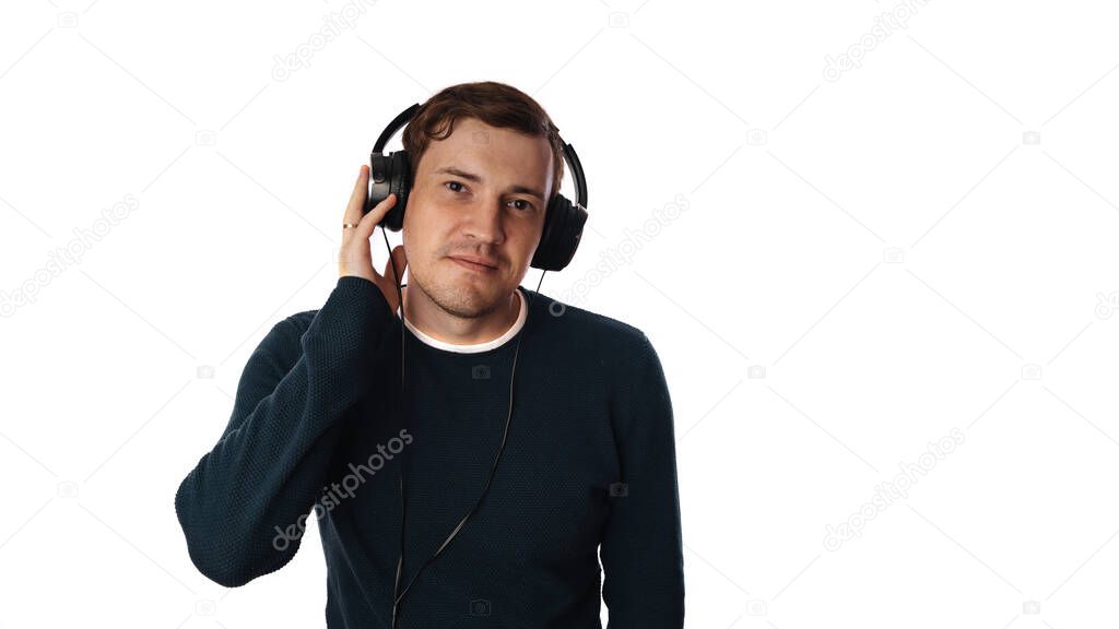A beautiful young man with bristles in a sweater and in headphones is smiling on isolated white background. Copy space.