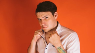 Beyaz gömlekli genç ve vahşi bir adam ellerini turuncu bir arka planda tutuyor..