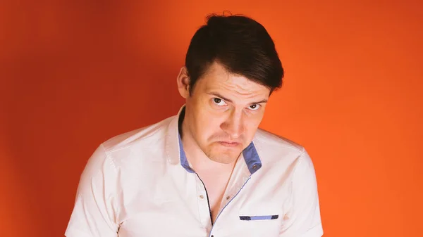 Un joven guapo con una camisa blanca se siente ofendido por algo o alguien sobre un fondo naranja . — Foto de Stock