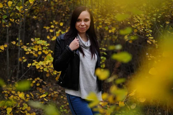 Портрет красивої усміхненої жінки стоїть в осінньому лісі між гілками дерев з жовтим листям . — стокове фото