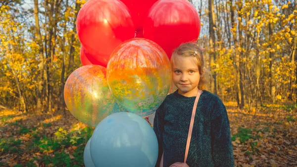 Ребенок гуляет по лесу со связкой разноцветных шариков. Девочка с цветными воздушными шарами в руке — стоковое фото