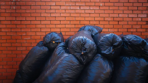 A big pile of garbage bags on the asphalt near a brick building. The concept of cleanliness and order in our environment. - Stock-foto