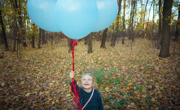 Маленькая девочка держит в руках воздушные шарики на прогулке по осеннему лесу. — стоковое фото