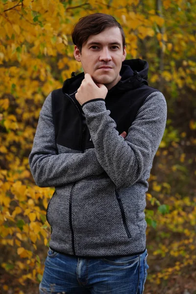 Retrato de um homem bonito jovem em roupas casuais contra as árvores amareladas na floresta de outono. — Fotografia de Stock