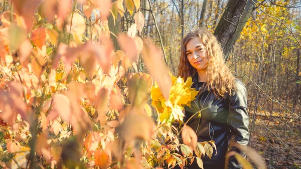 Портрет красивой улыбающейся женщины стоит в осеннем лесу между ветвями деревьев с желтой листвой. — стоковое фото