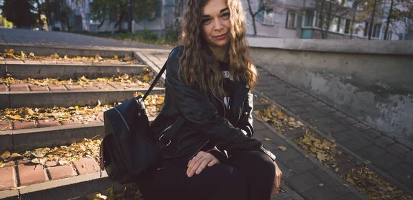 Молодая красивая женщина в повседневной одежде сидит на ступеньках с листьями в городском округе. — стоковое фото