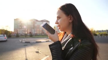 Bir kadın, şehir merkezinde bir caddede dururken akıllı telefon kullanarak bir sesli mesaj kaydediyor..
