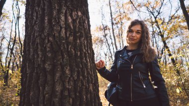 Ağacın arkasından bakan güzel bir kadın. Sakin bir kadın ağaca dokunuyor ve sessiz ormanda kameraya bakıyor.