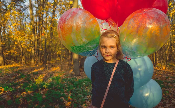 Маленькая девочка держит в руках воздушные шарики на прогулке по осеннему лесу. — стоковое фото