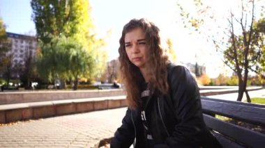 Güz parkındaki bankta günlük giysiler içinde genç ve güzel bir kadın oturuyor..