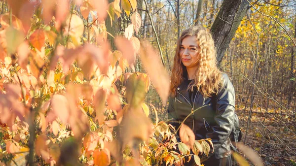 Portret van een mooie glimlachende vrouw staat in het herfstbos tussen de takken van bomen met geel blad. — Stockfoto