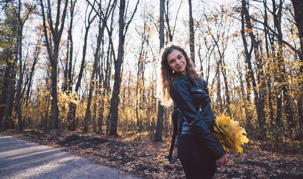 Junge Frau zwischen Bäumen. Porträt einer jungen attraktiven Frau, die im herbstlichen Garten steht und in die Kamera blickt — Stockfoto