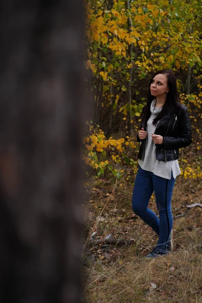 Retrato de uma mulher sorridente bonita está em pé na floresta de outono entre os ramos de árvores com folhagem amarela. — Fotografia de Stock