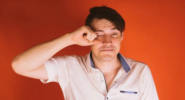 Um homem bonito novo em uma camisa branca esfrega seu olho no fundo laranja. — Fotografia de Stock