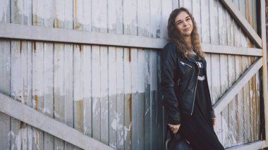 Günlük giysiler içinde güzel bir genç kadın paslı bir kapının arkasında poz veriyor..