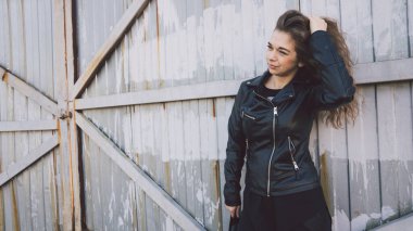 Günlük giysiler içinde güzel bir genç kadın paslı bir kapının arkasında poz veriyor..