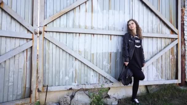 一个穿着休闲装的年轻貌美的女人正站在一个生锈的大门后面摆着姿势 — 图库视频影像