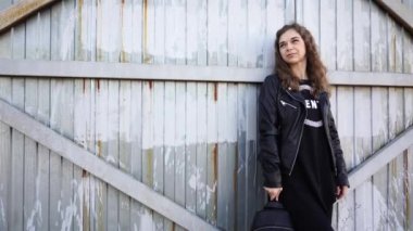  Gündelik giysiler içindeki güzel genç bir kadın paslı bir kapının arkasında poz veriyor.