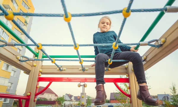Kinder spielen und toben auf dem Spielplatz. Ein Mädchen im blauen Pullover spielt im Hof eines mehrstöckigen Gebäudes — Stockfoto
