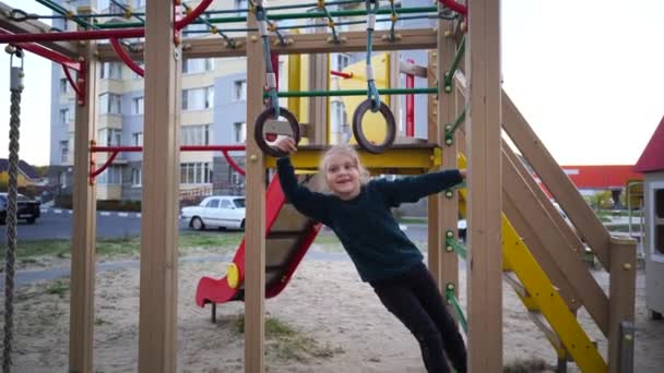 Jeu d'enfant et de rire sur le terrain de jeu. Une jeune fille portant un chandail bleu joue dans la cour d'un immeuble à plusieurs étages. — Video