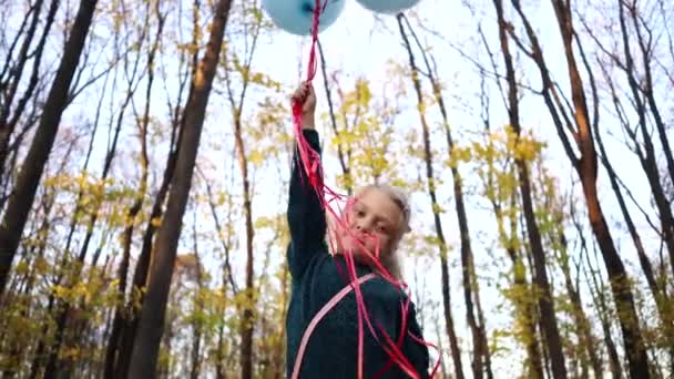 Ένα κοριτσάκι κρατάει μπαλόνια περπατώντας στο δάσος του φθινοπώρου.. — Αρχείο Βίντεο