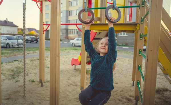 Kinder spielen und toben auf dem Spielplatz. Ein Mädchen im blauen Pullover spielt im Hof eines mehrstöckigen Gebäudes. — Stockfoto
