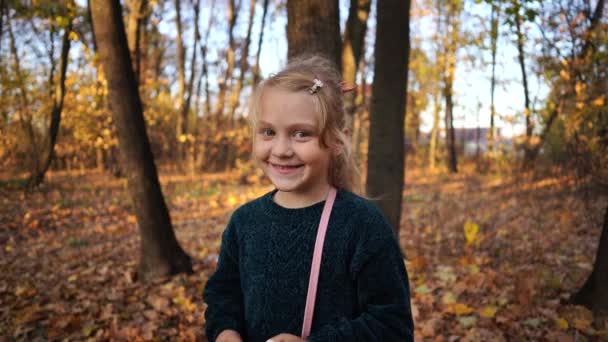 Una niña pequeña y tímida pinta sus labios en los bosques. Sumérjase en un sudor en el parque. Concepto: belleza y cosméticos — Vídeos de Stock