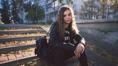 Gündelik giysiler içinde genç ve güzel bir kadın şehir merkezinde yapraklarla merdivenlerde oturuyor..