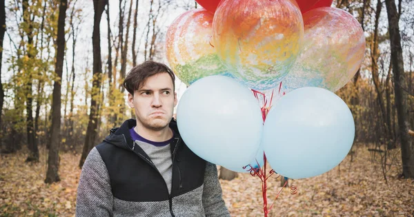 Un jeune homme beau tient les ballons colorés en promenade dans la forêt d'automne . — Photo