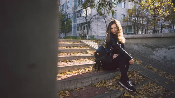 Молода красива жінка в повсякденному одязі сидить на сходах з листям у міському районі . — стокове фото