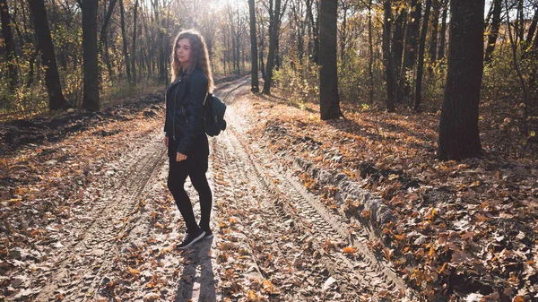 Женщина позирует стоящей в осеннем лесу. Девочка в кожаной черной куртке гуляет по лесу — стоковое фото