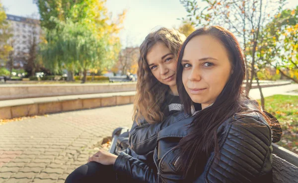 Zwei junge Frauen sitzen auf einer Bank im Herbstpark. Freundinnen trafen sich zum Wandern bei warmem Wetter. — Stockfoto