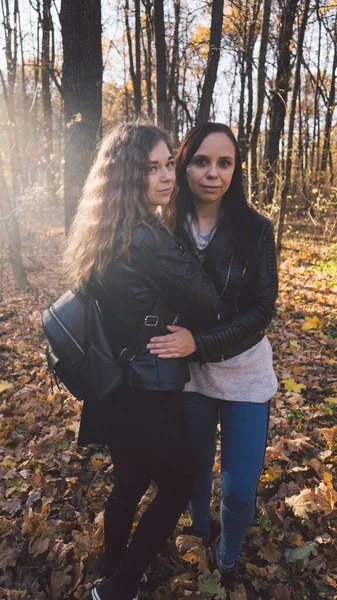 Två unga kvinnor kramas på en promenad i höstskogen. Flickvänner träffades för att gå i varmt väder. — Stockfoto