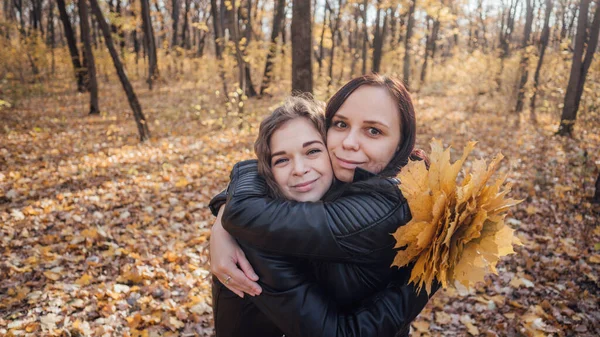 Zwei junge Frauen umarmen sich bei einem Spaziergang im herbstlichen Wald. Freundinnen trafen sich zum Wandern bei warmem Wetter. — Stockfoto