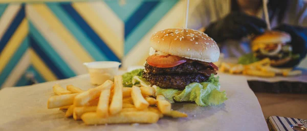 Szaftos hamburger két szelet sült krumplival. Egy finom hatalmas hamburgert. A gyorsétterem fogalma, a finom ételek, de egészségtelen.. — Stock Fotó