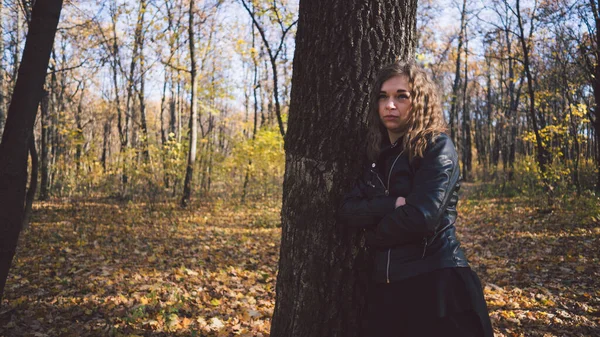 Jonge vrouw tussen de bomen. Portret van een jonge aantrekkelijke vrouw die in de herfsttuin staat en naar de camera kijkt — Stockfoto