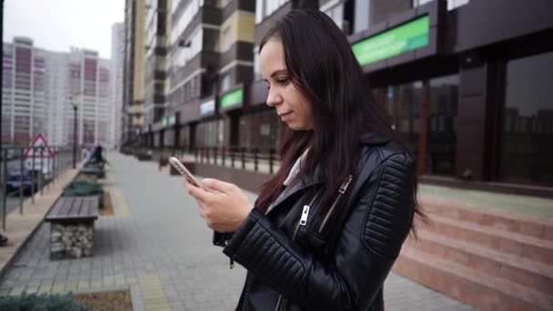 Una mujer escribe un mensaje usando un teléfono inteligente mientras está de pie. — Vídeo de stock