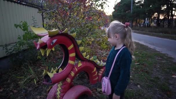 Una bambina affascinante in abiti casual si siede su una struttura dei pneumatici colorati in una campagna. — Video Stock